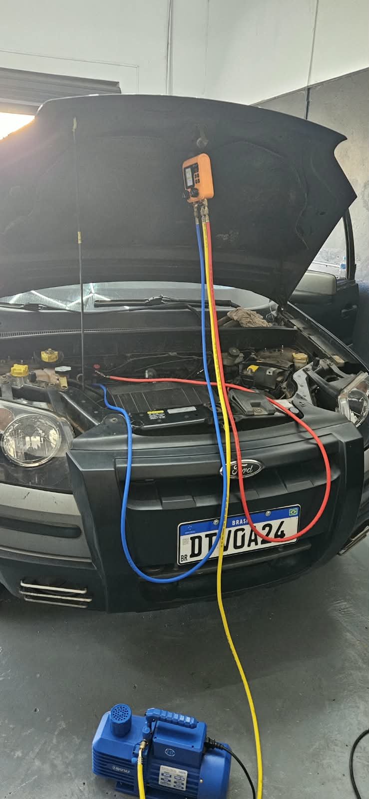 Manutenção do ar-condicionado de um Ford com medidor digital e mangueiras conectadas ao sistema